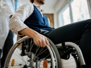 man in a shirt using a wheelchair with medical professional behind