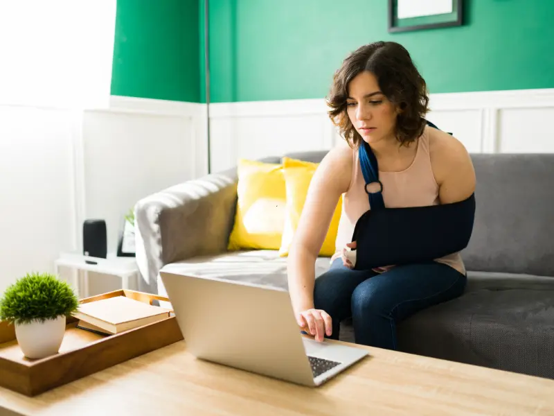 woman with arm in a sling works on a laptop